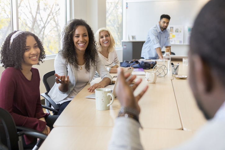 Mesa de reunião com três mulheres e dois homens ao redor, representando vaga inclusiva.