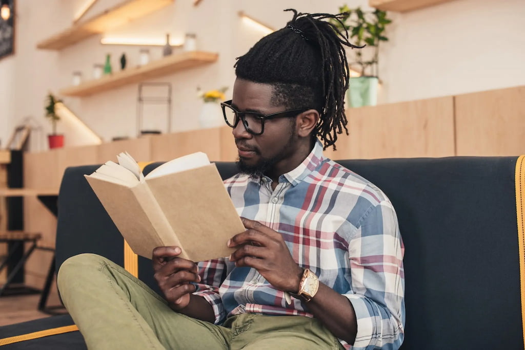 jovem negro sentado ao sofá lendo um livro, capa do conteúdo sobre livros sobre gestão de pessoas