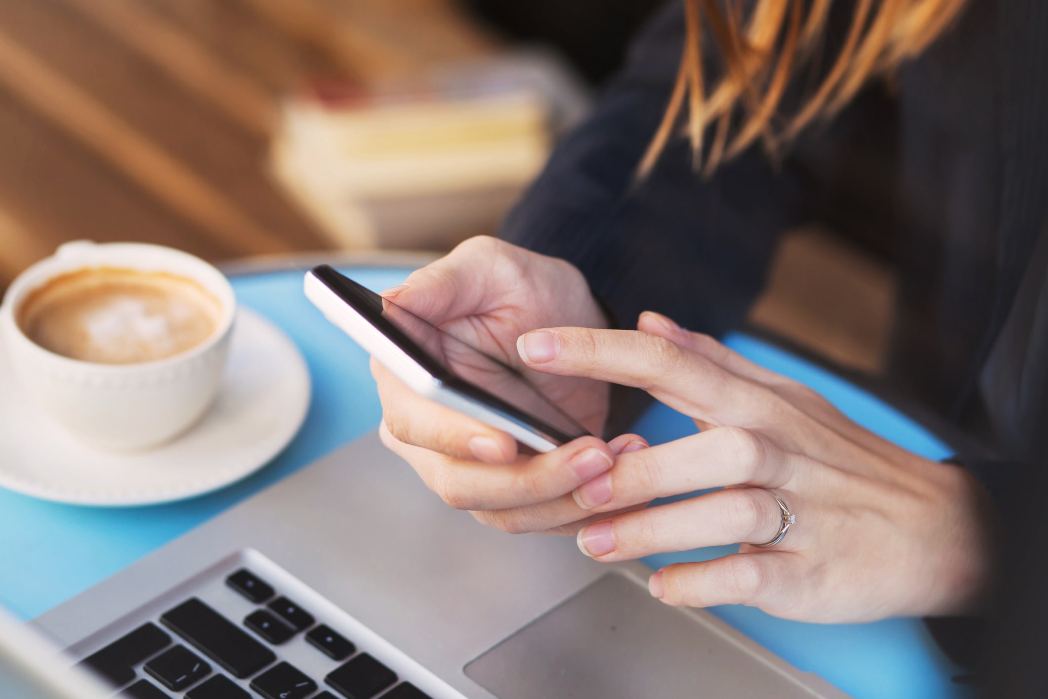 executiva toca no celular à sua frente está seu notebook aberto, ao lado, um taça de café