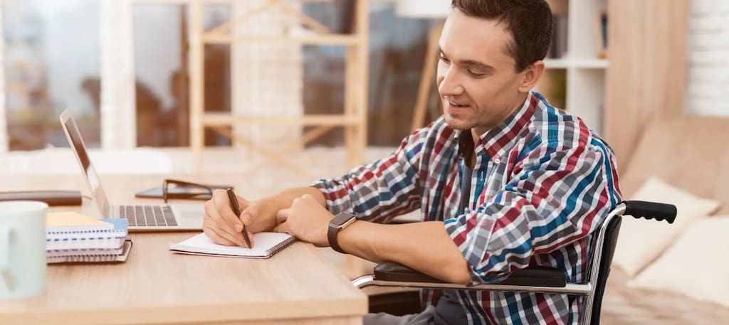 Homem cadeirante trabalhando no escritório e fazendo anotações em um bloco, capa do conteúdo sobre contratação de PCD