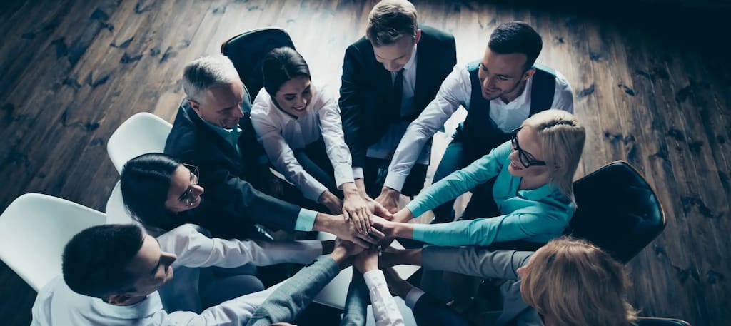 Equipe reunida em círculo unindo as mãos no centro em gesto de união e colaboração — capa do conteúdo sobre exemplos de cultura organizacional