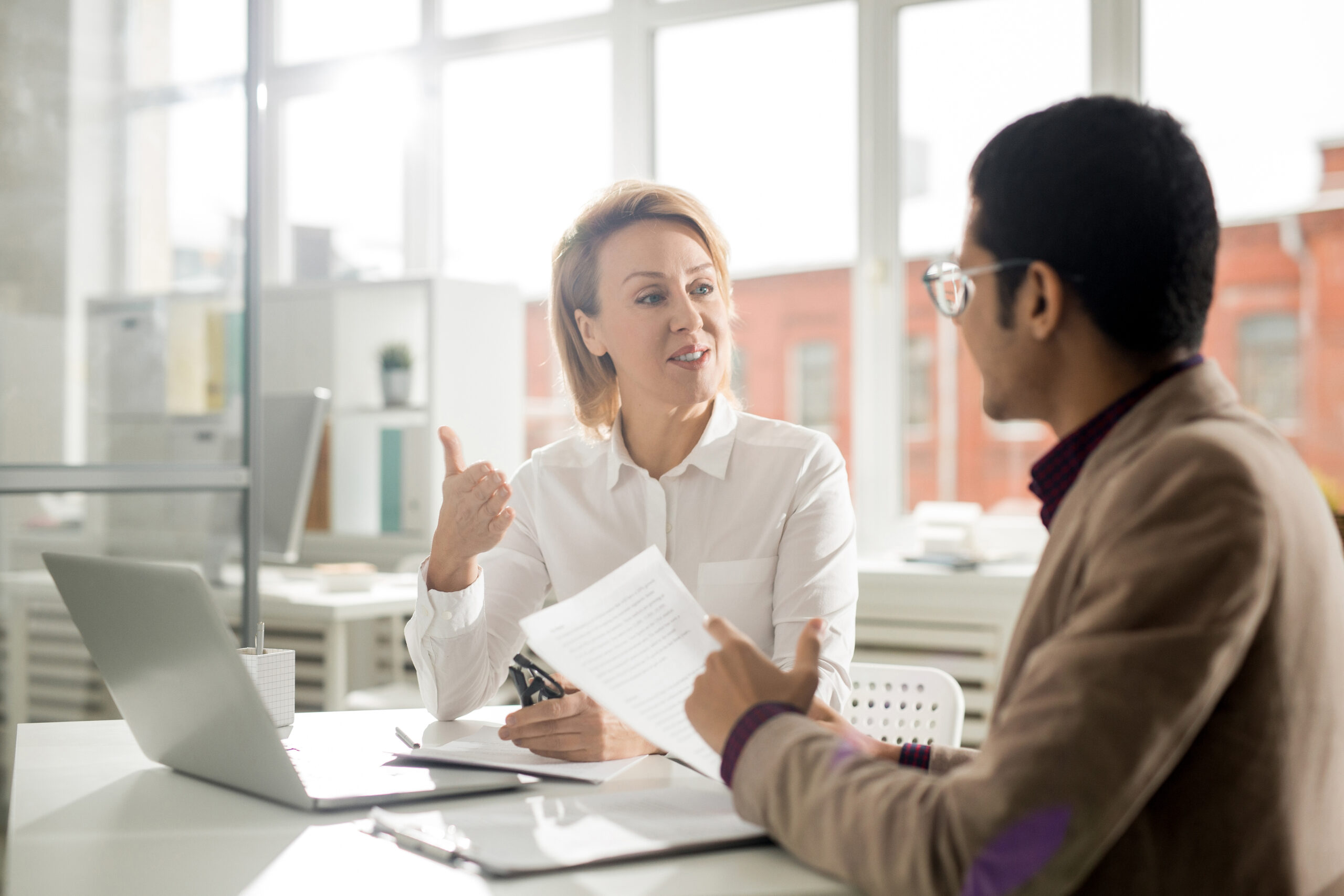 Um homem e uma mulher sentados em uma mesa de escritório conversando.